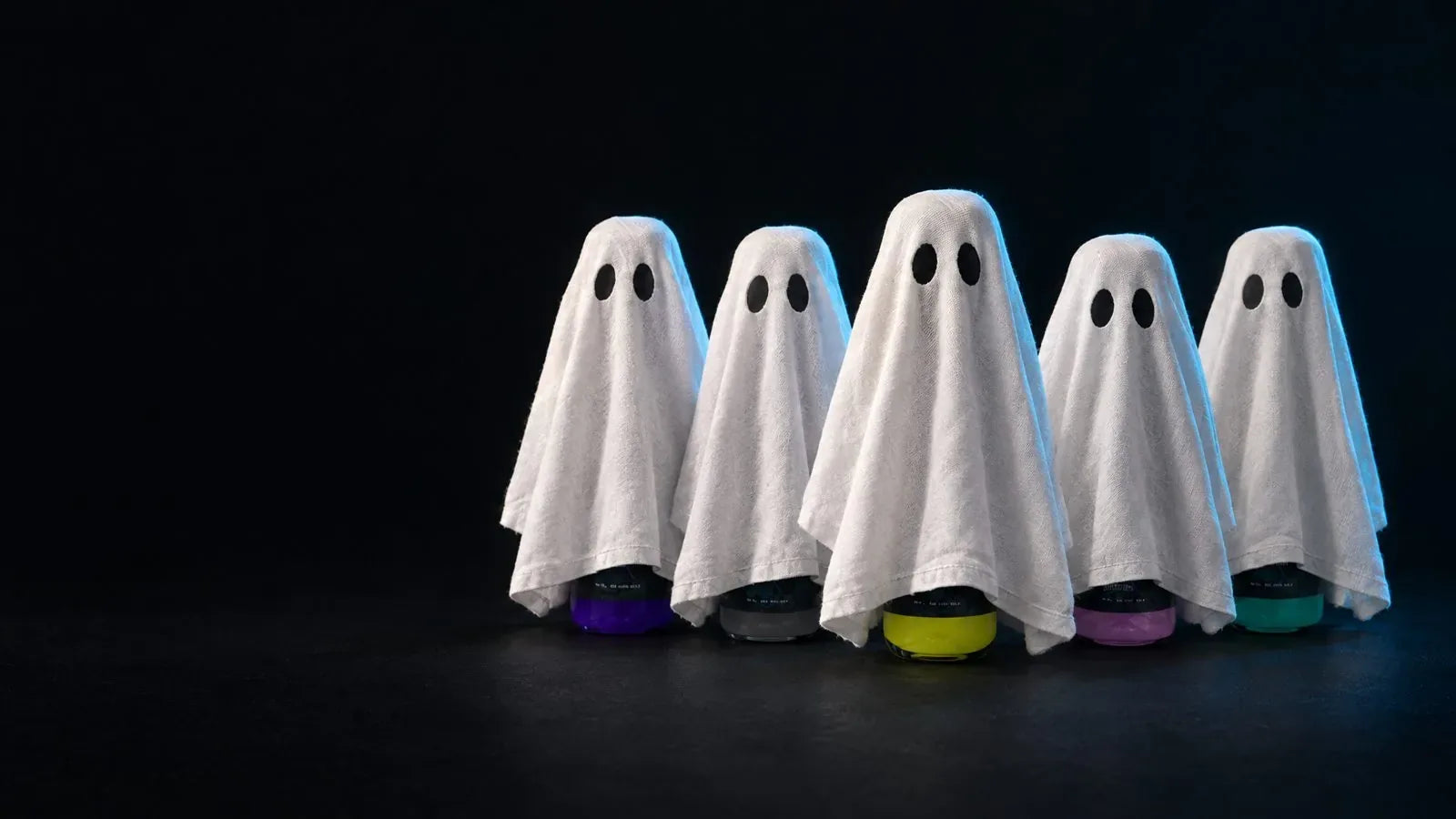Five ghost sheets on a dark set, colored Carbon Care bottle bases peeking out underneath